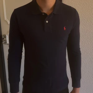 Marinblå pikétröja från Ralph Lauren - Säljer en stilren svart pikétröja från Ralph Lauren med klassisk krage och knappar. 