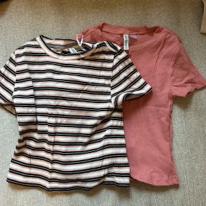 Randig och rosa ribbad topp - Två toppar till salu: en randig topp i svart, vit och rosa med korta ärmar och en rosa ribbad topp med korta ärmar. Perfekta för en avslappnad stil. 