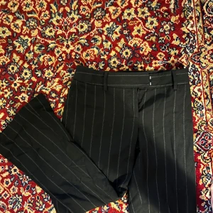 Svarta randiga kostymbyxor - Snygga svarta kostymbyxor med diskreta ränder. Byxorna har en klassisk passform och är perfekta för en stilren look. De har en dragkedja framtill och är tillverkade i ett bekvämt material.