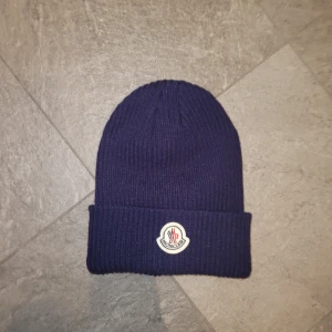 Mörkblå stickad mössa från Moncler - Snygg mörkblå stickad mössa från Moncler med ribbad design och broderad logotyp framtill. Perfekt för kyliga dagar. Inga byten. Priset kan diskuteras.