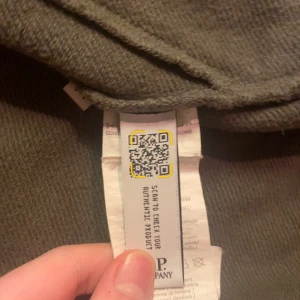 Grön jacka med glasögon från C.P. Company - Säljer en unik grön jacka från C.P. Company med inbyggda glasögon i huvan. Jackan har dragkedja framtill och är långärmad. Perfekt för dig som vill ha en stilren och funktionell look.