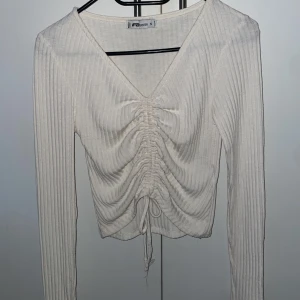 Vit ribbad tröja från FB Sister - Säljer en snygg vit ribbad tröja från FB Sister. Tröjan har en v-ringad design med snörning framtill som ger en cool look. Perfekt för att styla med jeans eller kjol. Passar bra till både vardag och speciella tillfällen.