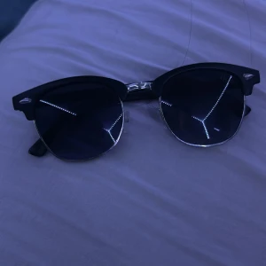 Svarta solglasögon från Ray-Ban - Snygga svarta solglasögon från Ray-Ban med klassisk design. De har en svart båge och mörka glas som ger en cool look. Perfekta för soliga dagar och en stilren outfit.