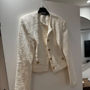 Vit kavaj med knappar - Snygg vit kavaj från Gina Tricot med en stilren design. Den har långa ärmar och knappar framtill samt två fickor. 💕