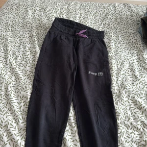 Svarta träningsbyxor från Stay Fit - Svarta träningsbyxor från Stay Fit med elastisk midja och lila snörning. Perfekta för träning med bekväm passform och stilren design.