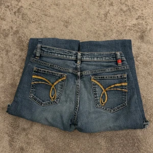 Blå bootcut jeans med broderade bakfickor - Snygga blå bootcut jeans med unika broderade detaljer på bakfickorna. Midjemått (rätt över):35cm Innerbenslängd:73cm Lårmått (rätt över):21cm 