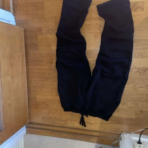 Svarta mjukisbyxor med broderad detalj - Svarta mjukisbyxor med broderade bokstäver på framsidan. Byxorna har en bekväm passform och dragsko i midjan för justerbarhet. Perfekta för en avslappnad stil.