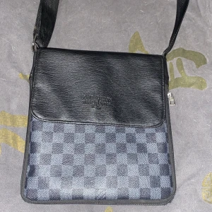 Svart och grå axelväska med rutigt mönster - Snygg axelväska i svart och grått med ett klassiskt rutigt mönster. Väskan har en justerbar axelrem och en praktisk dragkedja för säker förvaring. Perfekt för att bära med sig det viktigaste med stil.