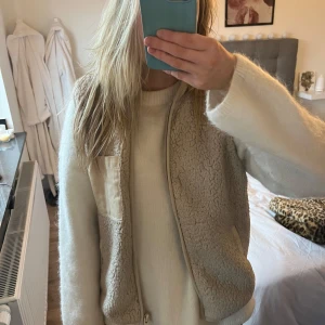 Beige fleeceväst med dragkedja - Säljer en mysig beige fleeceväst med dragkedja och en praktisk ficka framtill. Perfekt för lager-på-lager under kyliga dagar. Västen har en enkel och stilren design. Passar mig som är en S, lite fläckar som nog går bort i tvätten.