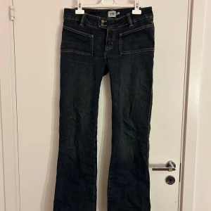 Mörkblå jeans  - Säljer ett par supersnygga mörkblå jeans från Lager 157! De är lågmidjade och har två knappar framtill som är lite på sidan. De är även bootcut. De har ett slitage mellan benen som visas på bild 4, lätt att sy ihop.