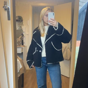 Svart teddyjacka med vita detaljer - Mysig svart teddyjacka med kontrasterande vita sömmar. Perfekt för kyliga dagar när du vill vara både varm och stilren. Nypris, köpt för 899