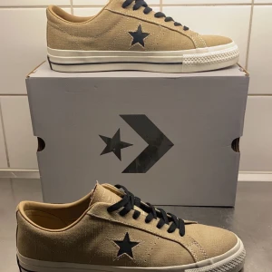 Converse skor - Snygga beige sneakers från Converse med svart stjärndetalj på sidan. Skorna är helt oanvända och har aldrig kommit till användning. Box o snöre ingår. Bara att skriva ifall du har frågor eller funderingar :)