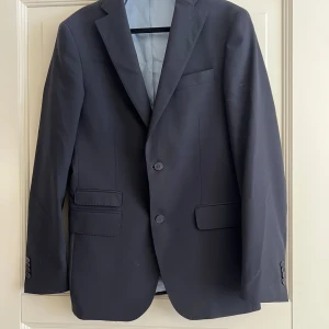 Svart kavaj från Cavaliere - Elegant svart kavaj från Cavaliere i storlek 46. Kavajen har en klassisk design med två knappar framtill och fickor med lock. Perfekt för formella tillfällen. Ej tvättad. 