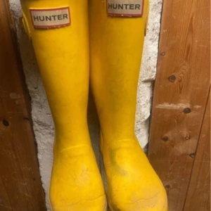 Gula stövlar från Hunter - Säljer ett par klassiska gula stövlar från Hunter. Perfekta för regniga dagar med sin höga design och slitstarka material. De har en ikonisk logotyp framtill och är lätta att rengöra.