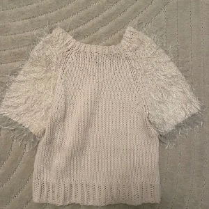 Beige stickad tröja med fluffiga ärmar - Säljer en unik beige stickad tröja med korta, fluffiga ärmar. Perfekt för att ge en extra touch till din outfit. Tröjan har en rund hals och är gjord i ett mjukt material som känns skönt mot huden.