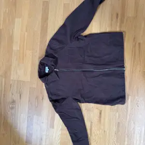 Säljer en stilren brun jacka från Weekday med dragkedja framtill. Jackan har en klassisk krage och en bröstficka. Perfekt för en avslappnad look.