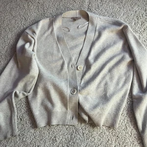 Beige kofta från H&M - Säljer en stilren beige kofta från H&M. Den har en klassisk design med knappar framtill och ribbade muddar vid ärmslut och nederkant. Perfekt för lager-på-lager under kyligare dagar. 🧥  