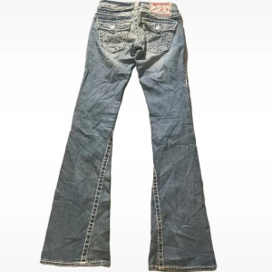 Blå bootcut jeans från True Religion - Snygga blå bootcut jeans från True Religion med klassiska bakfickor och detaljerade sömmar. St 24 några mindre fläckar som ska blrt med tvätt. Mått. Midja 32cm innerben 84cm