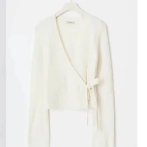 Vit omlottkofta från & Other Stories - Säljer en stilren vit omlottkofta från & Other Stories. Koftan har långa ärmar och en knytning i sidan som ger en elegant look. Perfekt för lager-på-lager under kyligare dagar. 🧣