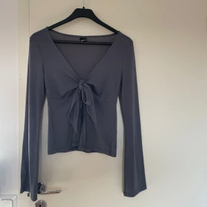 Grå blå långärmad topp med knyt - Snygg grå blå långärmad topp från Gina Tricot med knyt framtill. Nyskick aldrig använd. Toppen har en v-ringad design och är tillverkad i ett mjukt material.