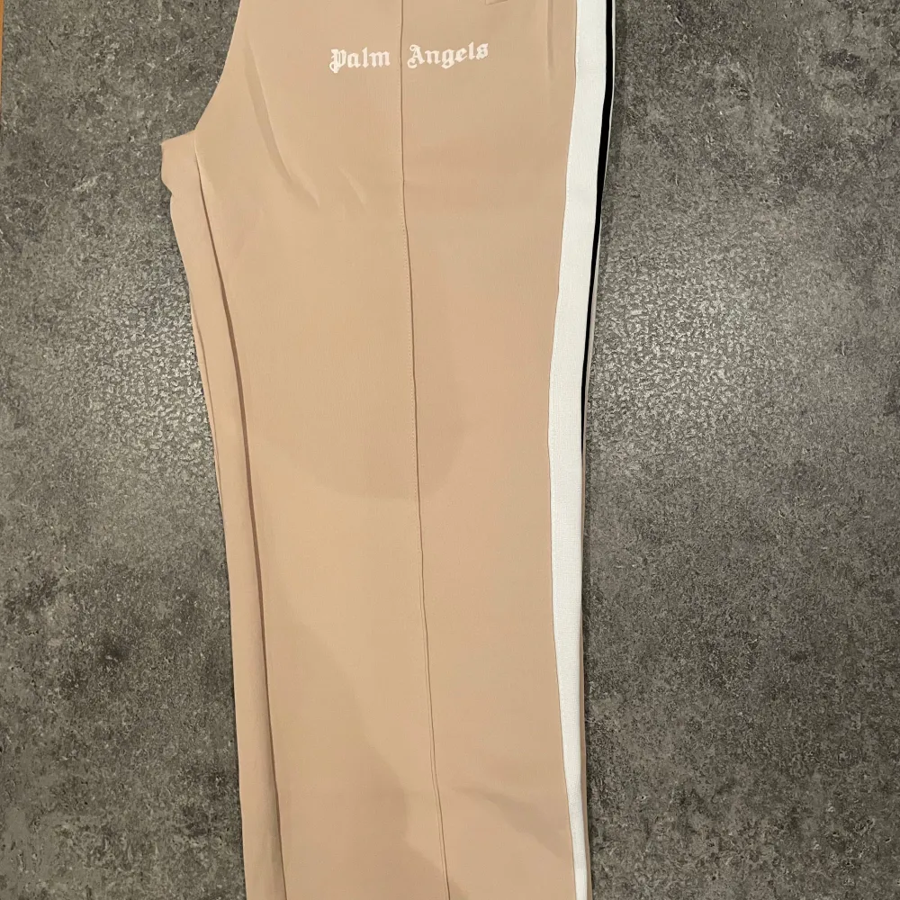 Snygga beige byxor från Palm Angels med vit sidoremsa. Perfekta för en stilren look. Byxorna har en normal passform och är tillverkade i ett bekvämt material.. Farkut & Housut.