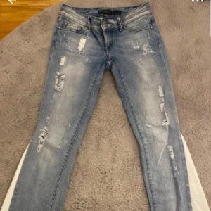slitna jeans - Säljer ett par blå jeans med slitningar. Är glitter i vissa slitningar. Knappen sitter löst men inget som mörkers när man bär jeansen. Prislappen kan diskuteras vid snabbt köp.💕💕 midja rakt över är det 36cm och innerbenslängd är ca 82cm.❣️