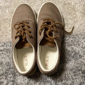 Bruna sneakers från Place - Snygga bruna sneakers från Place med snörning och vit sula. Perfekta för en avslappnad stil. Skorna har en klassisk design med en bekväm passform.