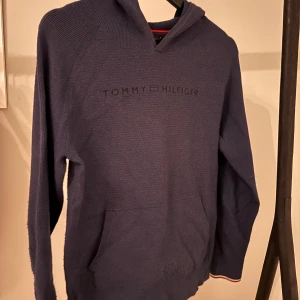 Mörkblå hoodie från Tommy Hilfiger - Säljer en snygg mörkblå hoodie från Tommy Hilfiger. Tröjan har en klassisk design med en känguruficka framtill och ribbade muddar. Perfekt för en avslappnad stil.