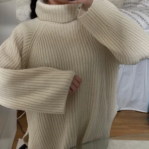 Beige stickad polotröja - Mysig beige stickad polotröja med ribbad struktur. Perfekt för kyliga dagar med sin höga krage och långa ärmar. En stilren och bekväm tröja som passar till det mesta. Oversized modell