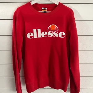 Röd tröja från Ellesse - Snygg röd tröja från Ellesse med deras ikoniska logga tryckt i vitt på framsidan. Tröjan har långa ärmar och en rund halsringning. Perfekt för en sportig och avslappnad stil.