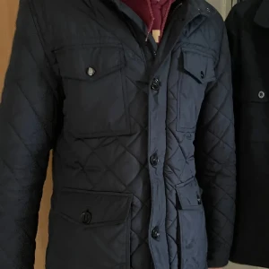 Mörkblå quiltad jacka från Tommy Hilfiger - Säljer en stilren mörkblå quiltad jacka från Tommy Hilfiger. Jackan har knappar och flera praktiska fickor framtill. Perfekt för kyligare dagar med sin klassiska design och bekväma passform.