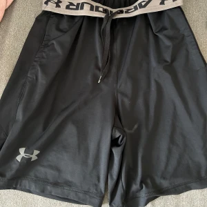 Svarta träningsshorts från Under Armour - Snygga svarta träningsshorts från Under Armour med elastisk midja och snörning för perfekt passform. Perfekta för gymmet eller löprundan. 