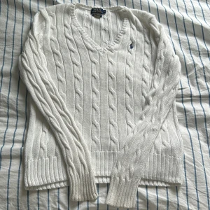 Vit kabelstickad tröja från Ralph Lauren - Säljer en klassisk vit kabelstickad tröja från Ralph Lauren i Pima bomull. Tröjan har en v-ringad design och det ikoniska broderade logotypen på bröstet. Perfekt för en stilren och tidlös look 💕🫶