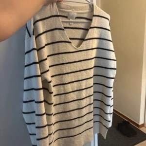 Randig beige tröja från H&M - Säljer en snygg beige tröja från H&M med svarta ränder och v-ringning. Tröjan har långa ärmar och är perfekt för en avslappnad stil. Passar bra till jeans eller kjol för en trendig look.