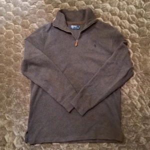 Brun tröja från Polo Ralph Lauren - Säljer en stilren brun tröja från Polo Ralph Lauren med dragkedja vid halsen. Tröjan har långa ärmar och en diskret broderad logga på bröstet. Perfekt för en avslappnad och snygg look.