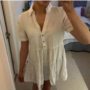 Vit kortklänning med knappar från Zara - Säljer en söt vit kortklänning med knappar framtill och korta ärmar från Zara