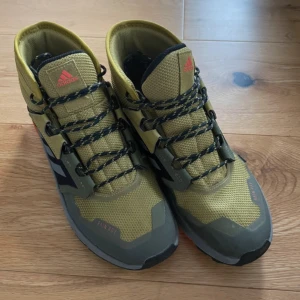 Adidas Terrex vandringsskor - Snygga Adidas Terrex vandringsskor i olivgrön och svart med orange detaljer. Skorna har en robust sula med bra grepp och snörning för optimal passform. Perfekta för utomhusaktiviteter och äventyr.