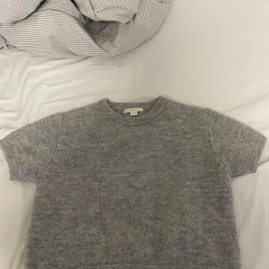 Grå stickad tröja från Gina Tricot - Mysig grå stickad tröja från Gina Tricot. Perfekt för kyligare dagar med sin mjuka och bekväma passform. Tröjan har korta ärmar och en rund halsringning.