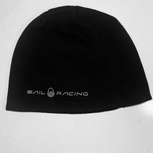 Svart Beanie | Sail Racing - Ge din look en sportig och exklusiv touch med Sail Racing Black Beanie. Tillverkad i högkvalitativt, stretchigt material för en perfekt passform och optimal värme under kalla dagar. Den stilrena med ikoniska Sail Racing-logotypen.