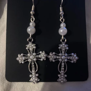 Silverfärgade korsörhängen med pärlor - Egengjorda Eleganta örhängen i form av kors, dekorerade med små pärlor och en större pärla ovanför. Perfekta för att ge en stilfull touch till din outfit. Skriv gärna om ni har frågor