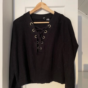 Svart stickad tröja  - Säljer en svart stickad tröja med snörning framtill och dekorativa öljetter. Ribbad