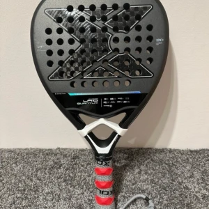 Padelracket NOX LP10 Quantum - Säljer ett NOX LP10 Quantum padelracket med 12K kolfiber. Racket har en modern design med svart och silver detaljer samt en perforerad yta för bättre kontroll. Perfekt för både nybörjare och erfarna spelare som söker precision och kraft.