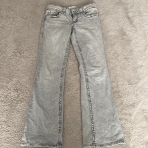 Grå bootcut low waste jeans från Gina Tricot - Snygga grå bootcut jeans från Gina Tricot. De har en klassisk bakficksdesign med knappar och dragkedja framtill. Perfekta för en stilren look med en touch av retro. Märkta som 'perfect jeans'.