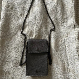 Svart axelväska från Coach - Snygg svart axelväska från Coach med en stilren design. Väskan har en kedjerem och en praktisk ficka på baksidan. Perfekt för att bära det viktigaste med stil.