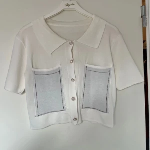 Vit kortärmad kofta med fickor - Säljer en stilren vit kofta med korta ärmar och knappar framtill. Den har två stora fickor med dekorativa sömmar. Perfekt för en avslappnad look.