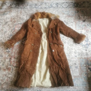 Brun mockakappa från Ernesto Modèles - Säljer en snygg brun mockakappa från Ernesto Modèles med pälsdetaljer på krage och ärmslut. Kappan har knappar framtill och en lång, elegant design. Perfekt för kyliga dagar när du vill hålla stilen. Pris kan själv klart diskuteras men går tyvärr inte längre ner än 700 eftersom det är en äkta päls jag fick från en familjemedlem för 1 år sedan. Jackan har blivit använd 1 gång, av mig iaf, men den passar inte riktigt min stil så säljer den och hoppas på någon som kommer bära den oftare än mig 