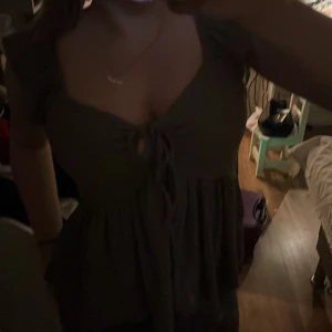 Brun ribbad topp med knytning - Säljer en brun ribbad topp med knytning framtill. Toppen har korta ärmar och en lätt volangdetalj nedtill. Perfekt för en avslappnad stil.