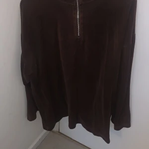 Brun manchestertröja från Enjoy Life - Säljer en brun manchestertröja från Enjoy Life med dragkedja framtill. Tröjan har långa ärmar och en hög krage, perfekt för kyligare dagar. Den är både stilren och bekväm, ett måste i garderoben!