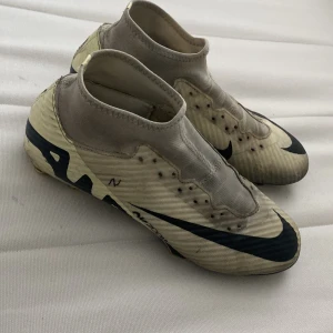 Nike fotbollsskor med svart swoosh - Säljer ett par Nike fotbollsskor i beige med svart swoosh. Skorna har en strumpliknande passform och är designade för optimal prestanda på planen. Perfekta för dig som vill ha stil och funktion i ett.