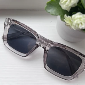 Transparenta solglasögon med svart lins - Snygga solglasögon med mörkgrå transparent båge och svarta linser. Den rektangulära formen ger en modern look. Perfekta för soliga dagar och en stilren accessoar till din outfit. Aldrig använda 🩶